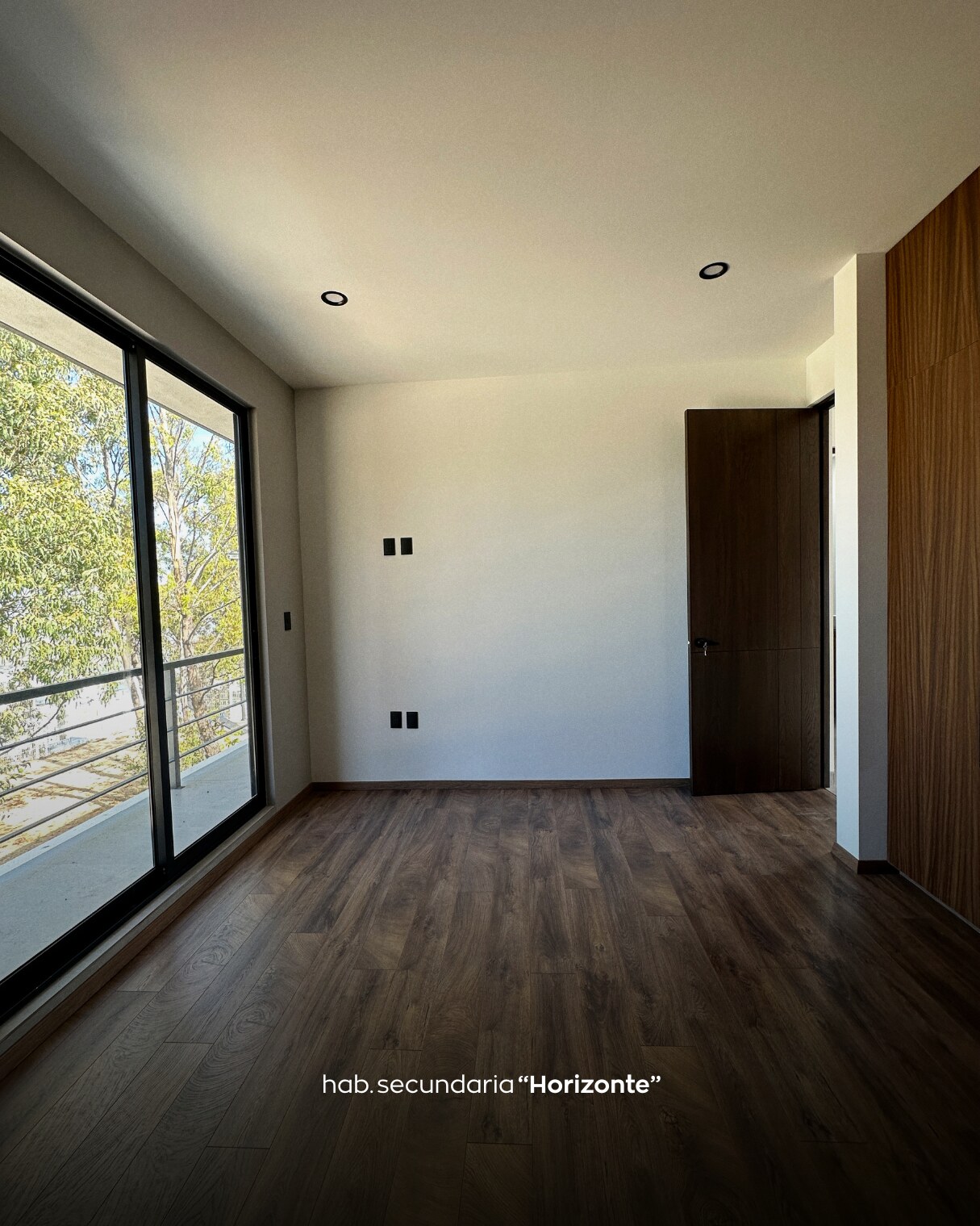 Habitación secundaria con piso de madera y ventana grande con vista a árboles · Casa Horizonte