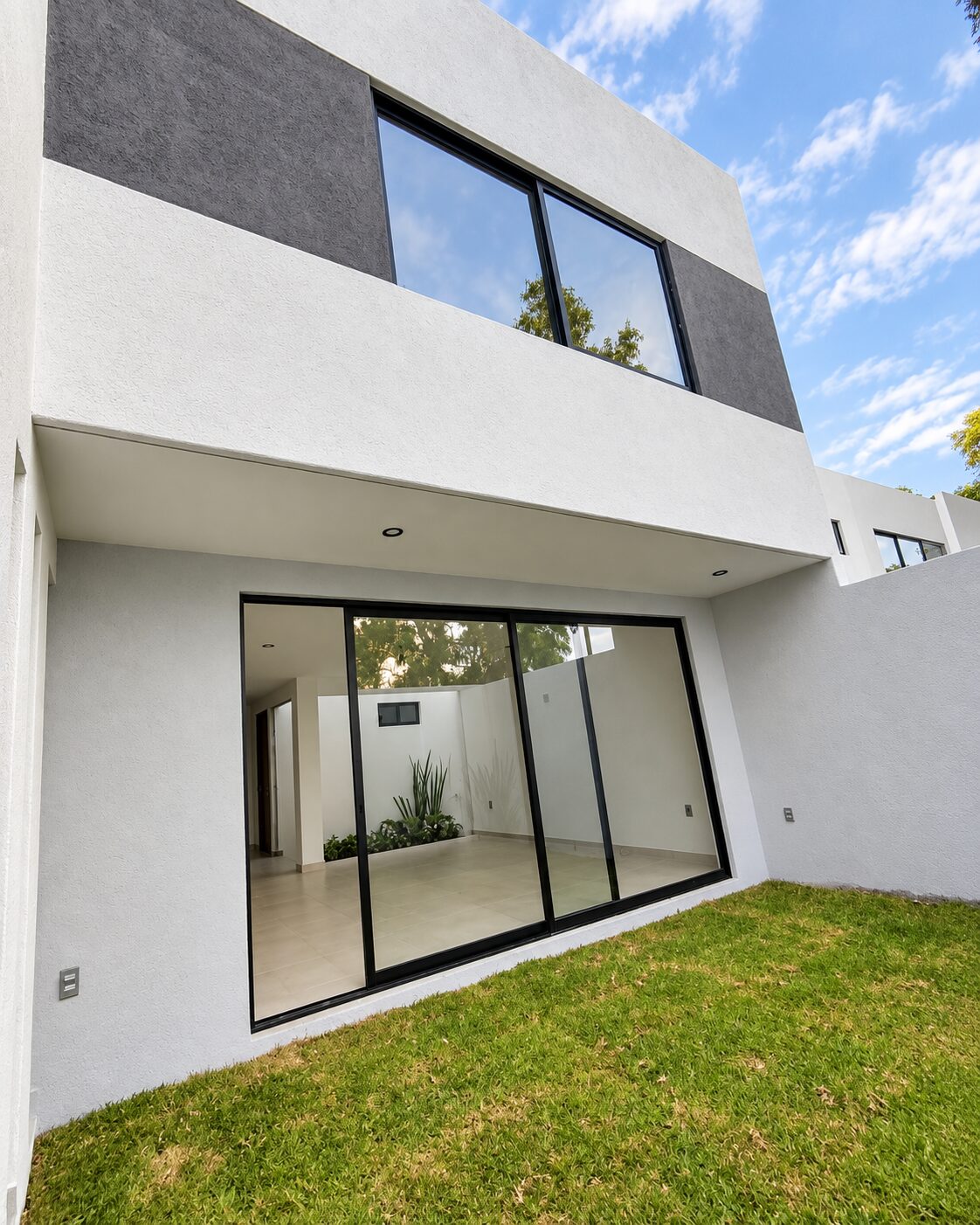 Fachada posterior con ventanal corredizo y jardín · Casa Magna por Mircon Constructora, constructores en Morelia